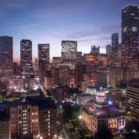 Twilight descends on a vibrant Texas city skyline, with illuminated buildings and a historic dome-structured edifice in the foreground.