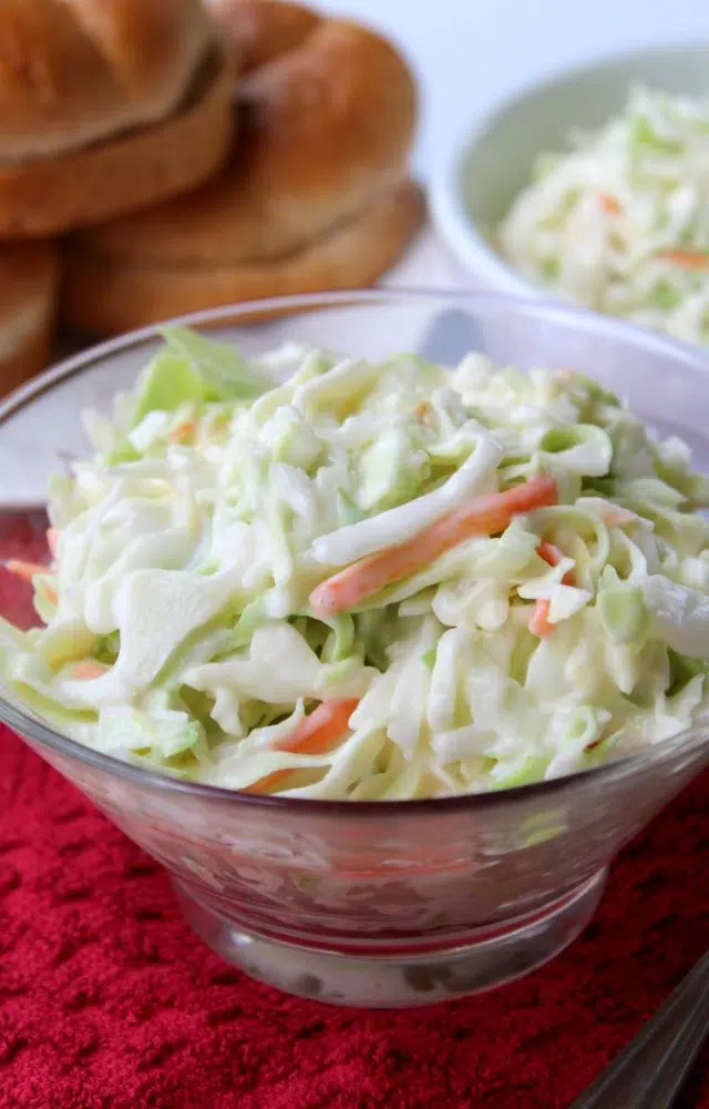 A bowl of creamy Chick-Fil-A Cole Slaw Recipe with sliced carrots, served alongside bread rolls.