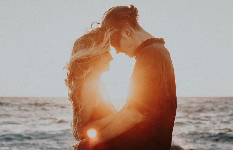 A man and woman standing on beach at sunset hugging