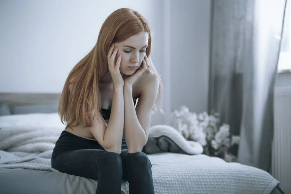 woman sitting on bed with hands on face