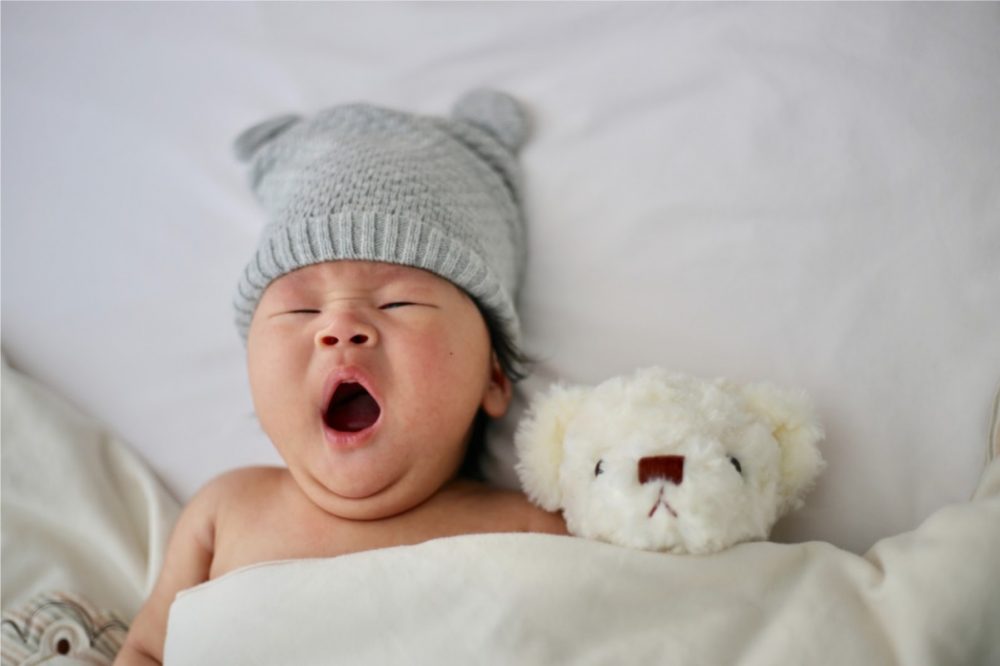 baby laying in back yawning with a stuffed animal next to him