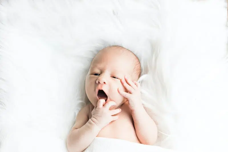 baby laying on white blanket on back with finger in mouth