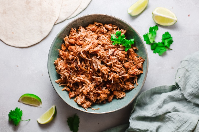 Instant Pot Mexican Carnitas in a blue bowl with tortillas 