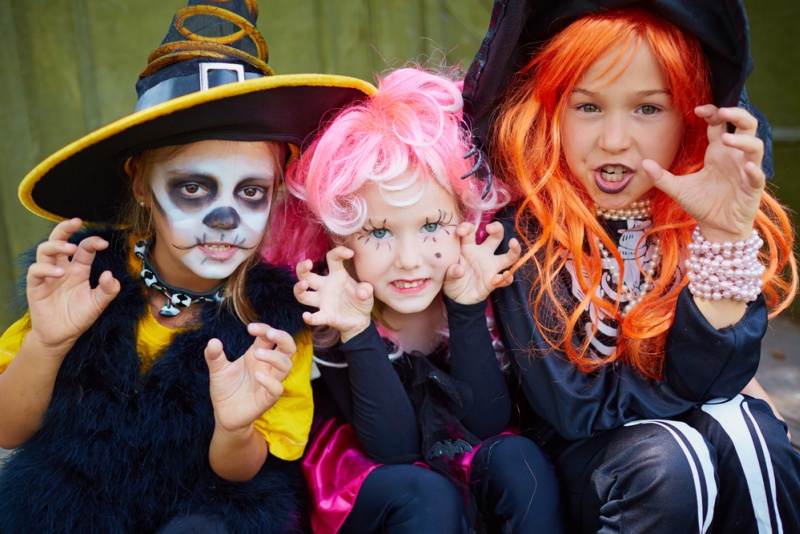 Portrait of three little girls in Halloween costumes looking at camera with frightening gesture