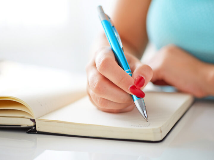 Young woman writes to black diary on a white table