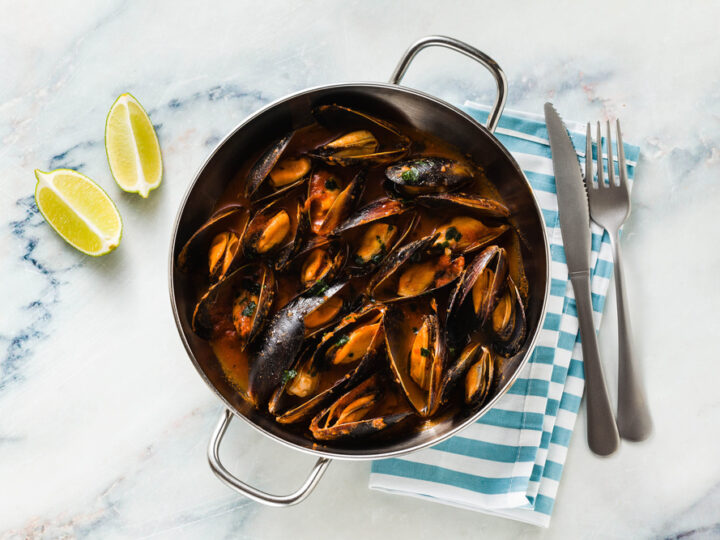 freshly cooked mussels in a frying pan in tomato sauce. pepata di cozze or mussels marinara. classic dish of mediterranean italian cuisine on white with blue marble table