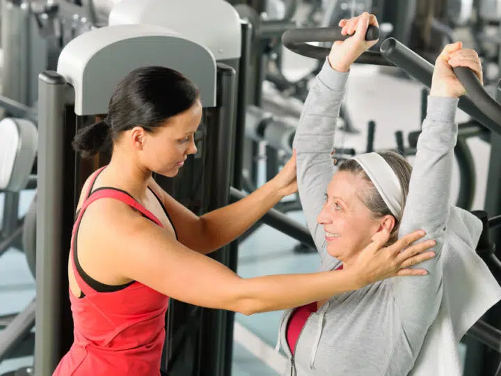 Senior woman exercise on shoulder press machine with personal trainer