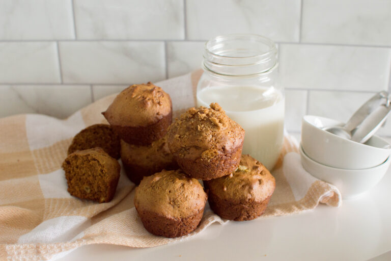 Homemade gingerbread muffins on a square white plate, sitting on a wire rack with a plaid napkin and a glass of milk
