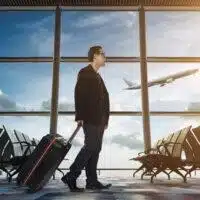 A man with a suitcase considers his travels in an airport waiting room.