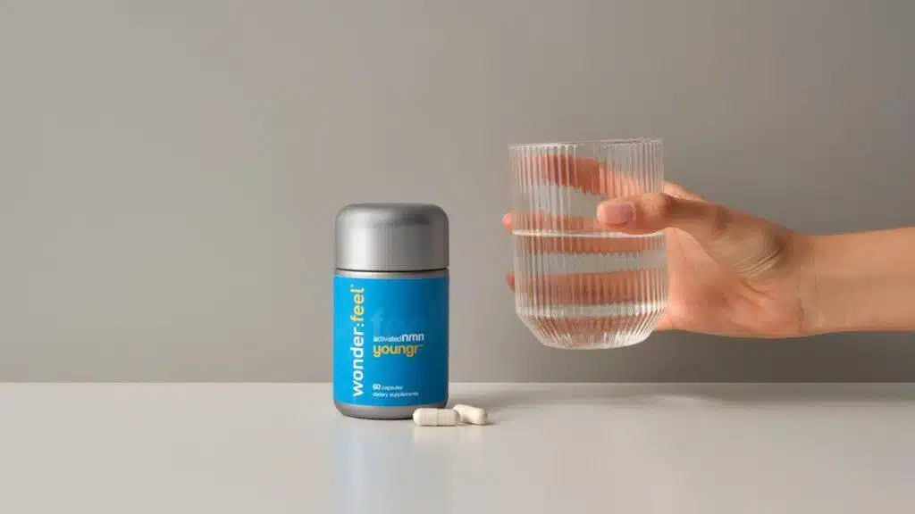 A person holding a glass of water next to a bottle of dietary supplements experiences the NMN benefits.