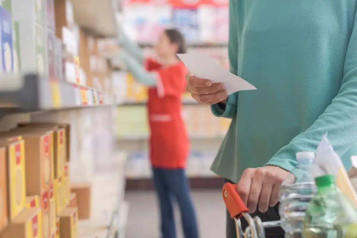 A person with a grocery cart reads a shopping list while another stocks shelves in the store aisle, transforming their routine shopping experience.