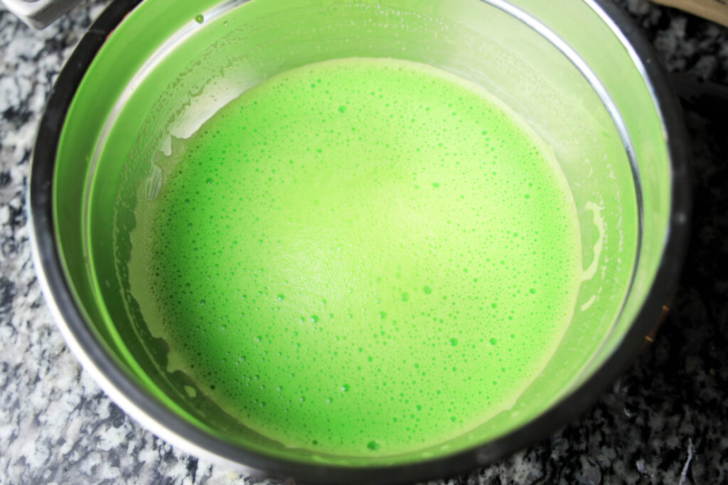 On a speckled countertop sits a metal bowl brimming with bright green, frothy liquid—an enticing start for your Mardi Gras jello shots recipe adventure.