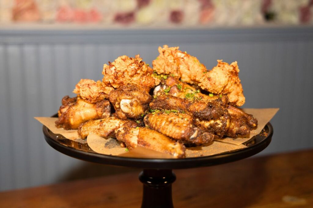 At The Ainsworth Hoboken, a plate piled with various fried chicken pieces sits invitingly on a wooden table, capturing the delicious essence of Hoboken restaurants.