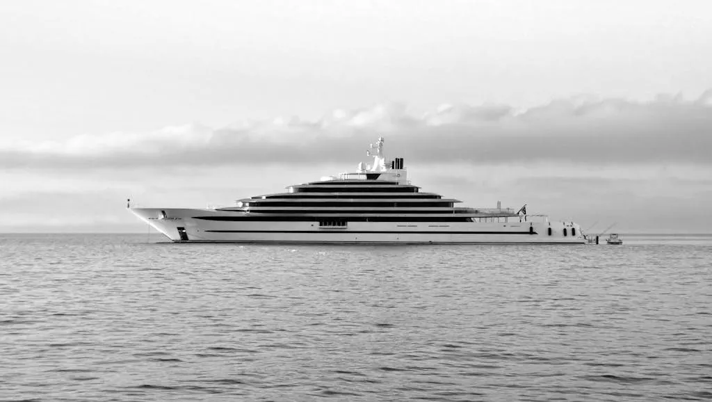 A sleek yacht cruising the calm ocean under a cloudy sky in monochrome beauty.