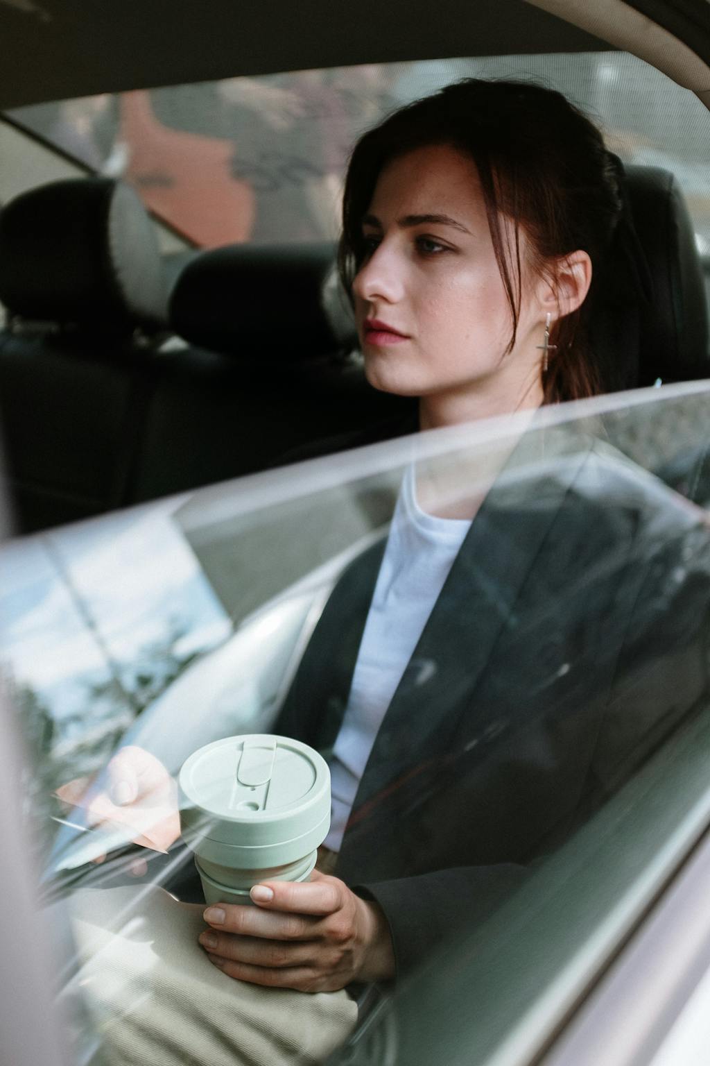 Thoughtful young woman holding coffee cup while commuting in car.