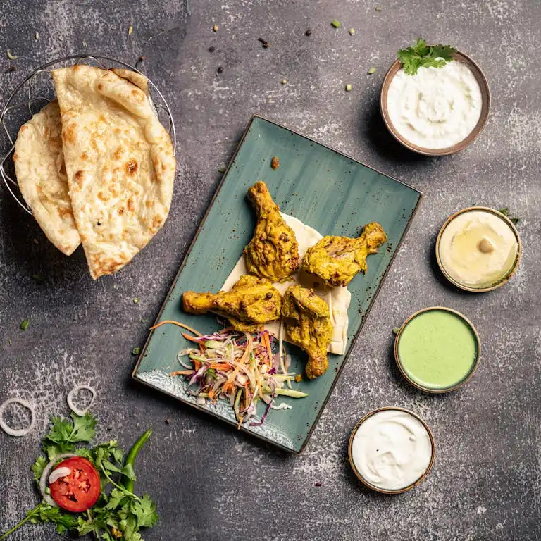 A vibrant Indian food platter featuring grilled chicken, naan bread, sauces, and fresh salad.