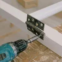 Close-up of an electric drill installing a door hinge on a wooden workbench.