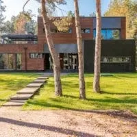 Contemporary house with large glass windows surrounded by lush greenery and a paved pathway.