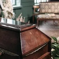 Elegant wooden coffin surrounded by floral arrangements in an indoor funeral setting, capturing a somber mood.