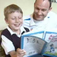 An adult and a child sit on a couch, smiling and reading a book together, highlighting the importance of early diagnosis in supporting children’s development.