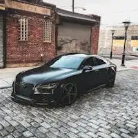 A sleek black car parked on a cobblestone street in an urban setting, featuring brick buildings.