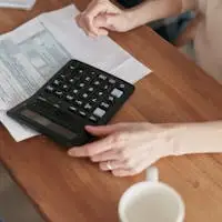 Focused individual using calculator to manage personal finances at wooden desk.