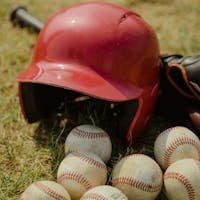 A red baseball helmet and multiple baseballs on a grass field, perfect for sports-themed designs.