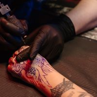 A tattoo artist wearing black gloves working on a detailed dragon design in a studio.