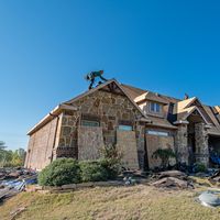 Brick house in Weatherford, Texas undergoing roof installation. Workers on roof under clear sky.