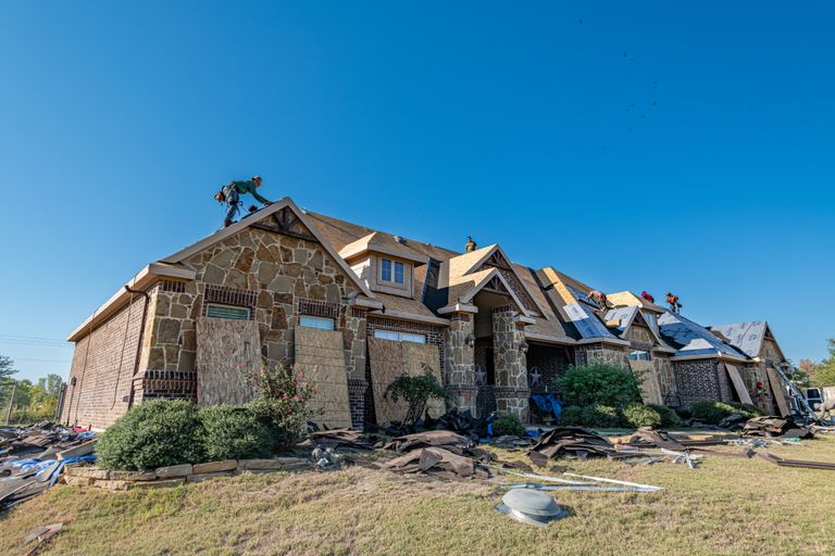 Brick house in Weatherford, Texas undergoing roof installation. Workers on roof under clear sky.