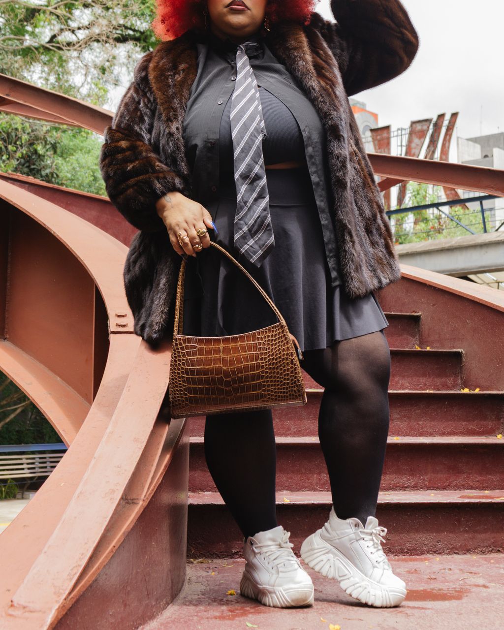 Stylish woman with pink hair, fur coat, and handbag on outdoor staircase in S&atilde;o Paulo.