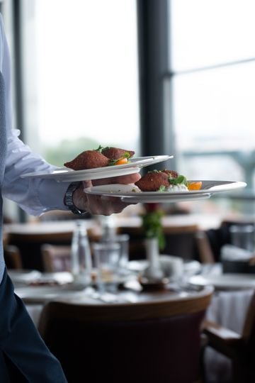 A waiter serves gourmet plates in a fine dining setting with blurred background.