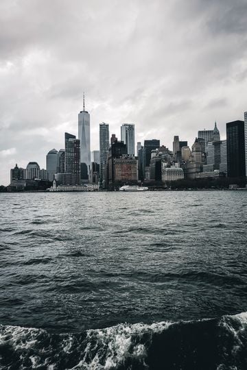 Dense city with futuristic skyscrapers and embankment in gloomy day with heavy clouds above rippling sea water